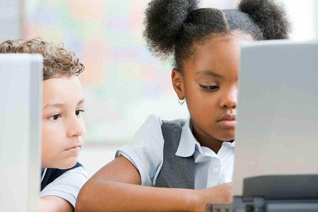 Two children focused on a computer screen in a colorful classroom.