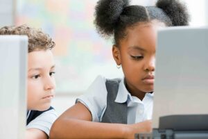 Two children focused on a computer screen in a colorful classroom.